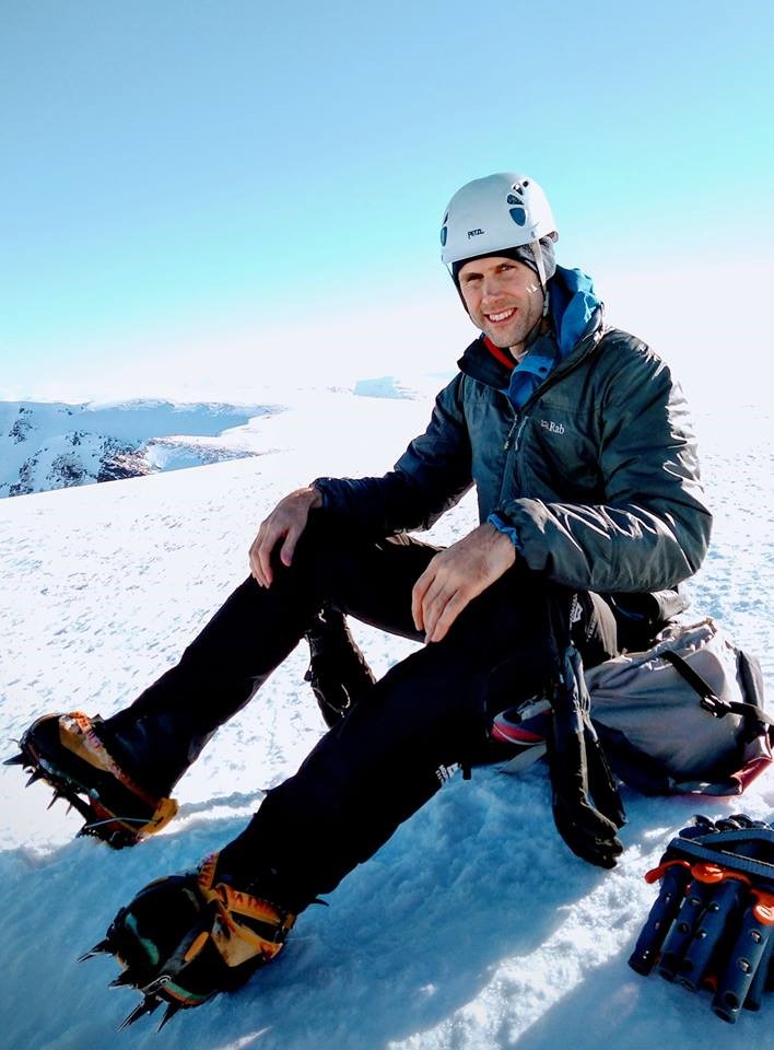 Climber sat on a snowy plateau in bright sunshine.